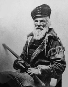 Elderly man with bear and hat holding a long barrel gun