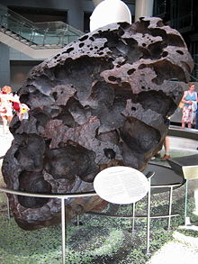 A large black egg)shaped boulder of porous structure standing on its top, tilted.