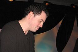 A man with black hair leans forward, looking down to sign an autograph.